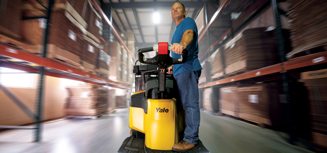 A warehouse worker rides an end rider down a warehouse aisle