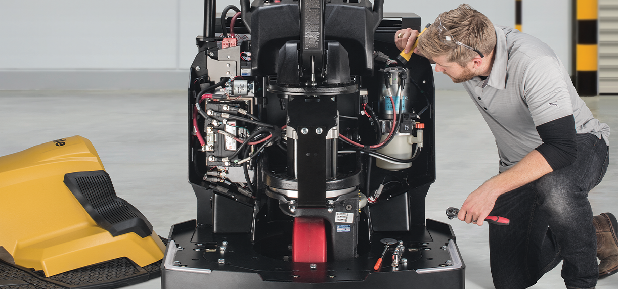 A maintenance technician kneels down to look at a Yale end rider&rsquo;s mechanical system