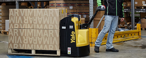 A warehouse worker pulls a Yale pallet truck with full pallet-load 