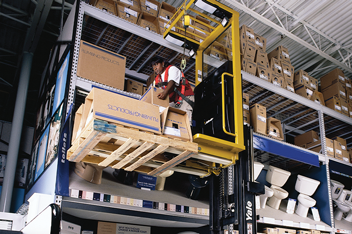 Order picker operator lifts a box onto a warehouse rack in the air