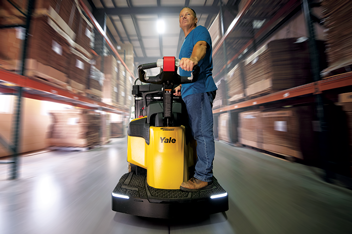 A warehouse worker rides an end rider down a warehouse aisle