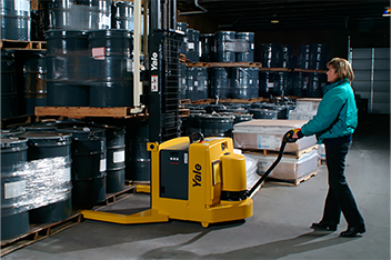 A female warehouse worker pushes a pallet stacker with full pallet load 