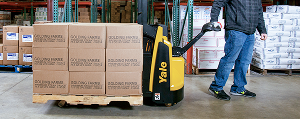 A warehouse worker pulls a Yale pallet truck with full pallet-load 