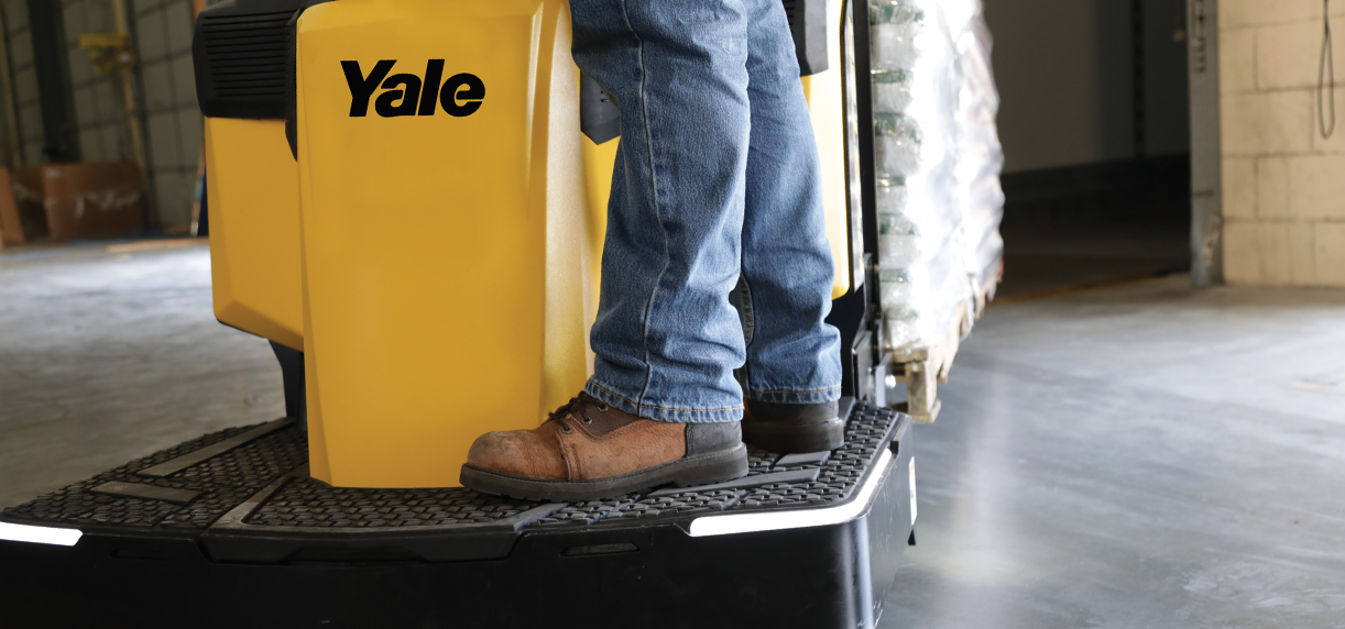 Close-up of a warehouse worker’s legs and
                        boots on a Yale end rider