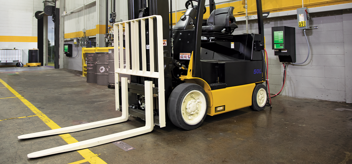 A forklift parked against a warehouse wall with its lithium-ion battery plugged into the wall