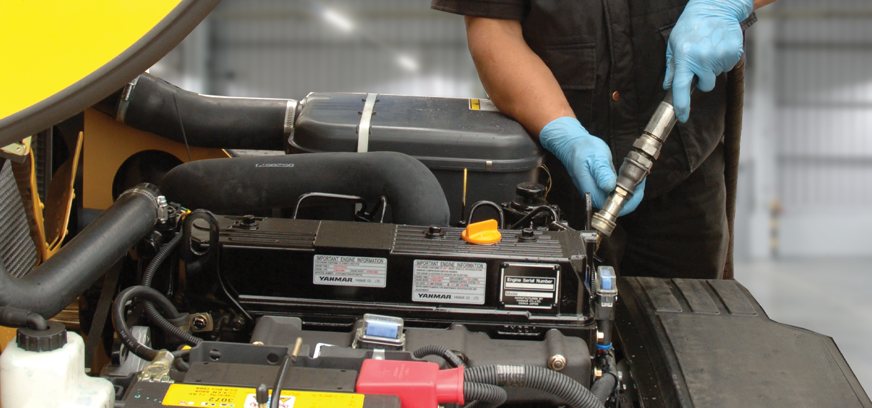 A maintenance technician adjusts part of a forklift engine with tool