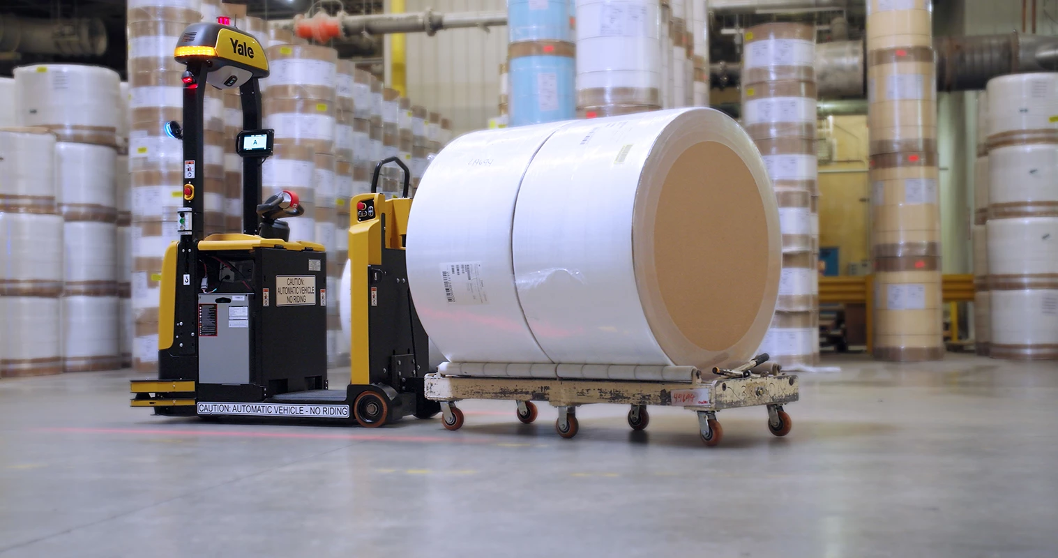 Yale Relay automated tow tractor transporting a paper roll on a flatbed cart